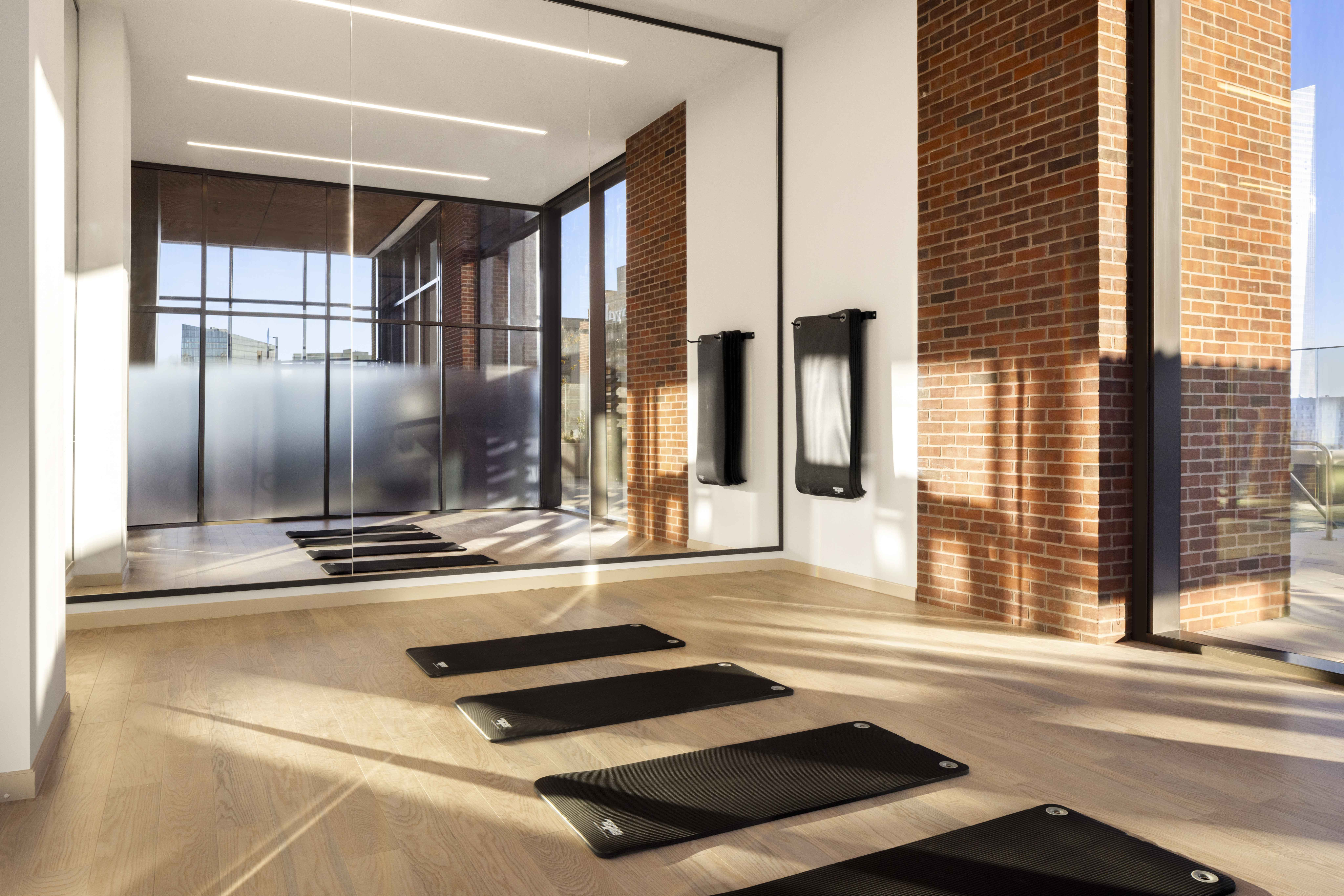 Modern yoga studio with wooden floors, mirrored wall, and picturesque urban view, featuring neatly arranged fitness mats.