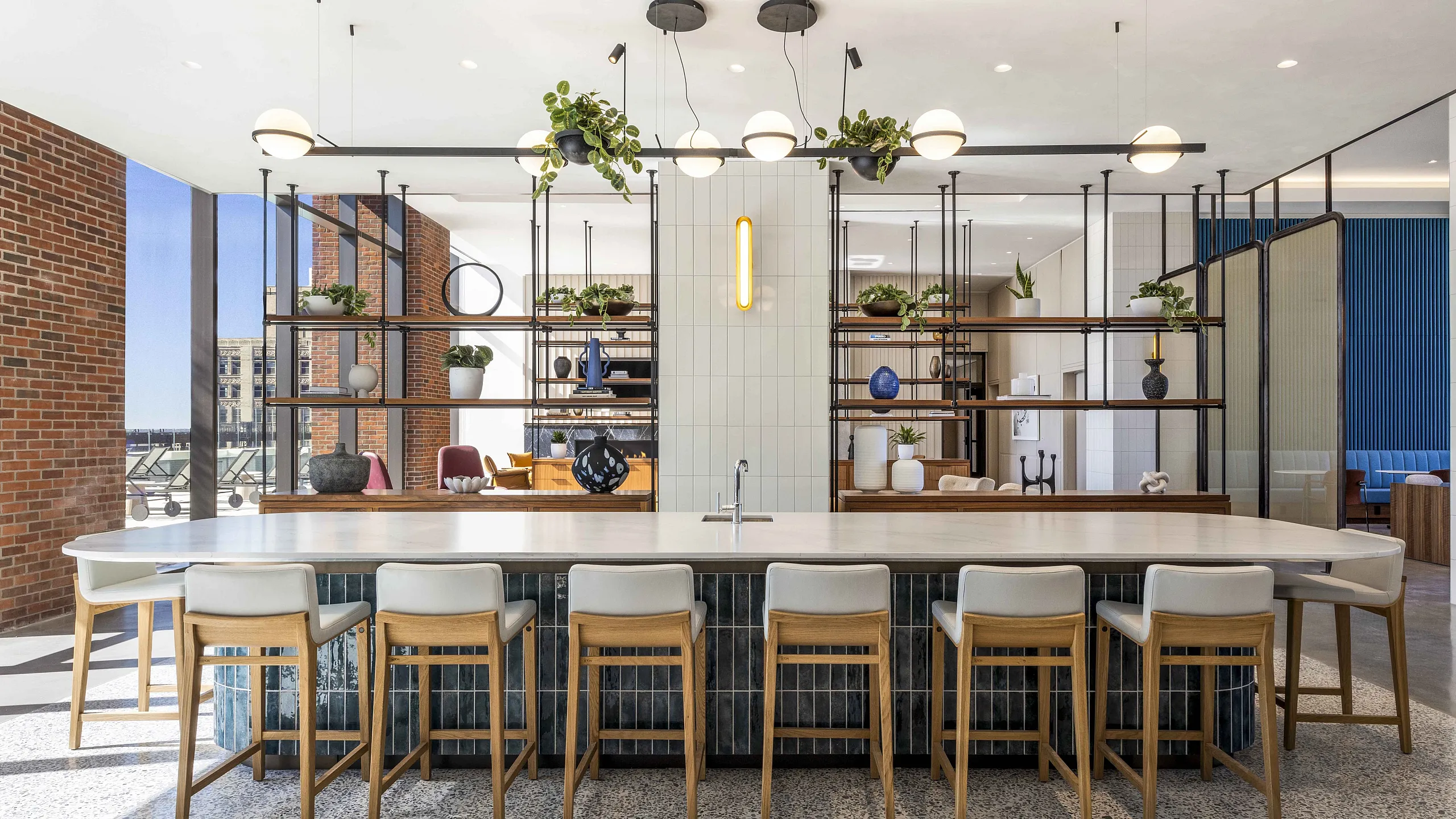 Elegant modern apartment lounge featuring a spacious open-plan layout, sleek countertop bar with stylish stools, and contemporary light fixtures under natural light from large windows.