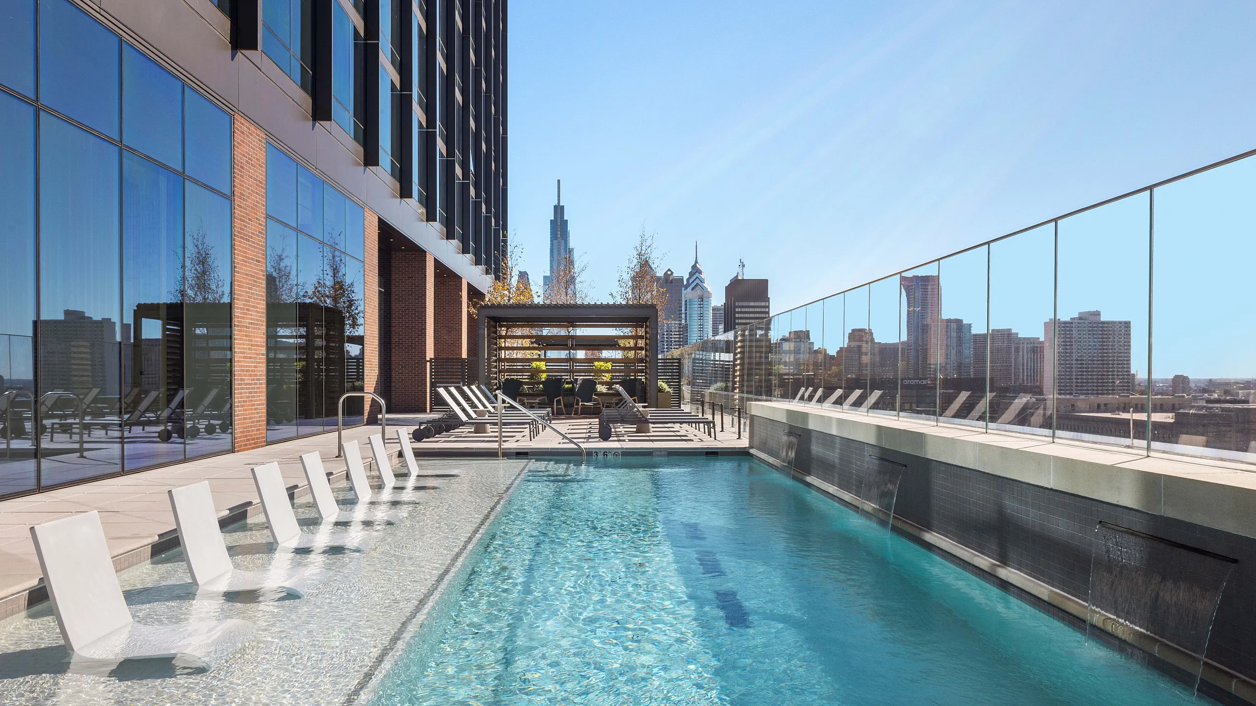 Luxurious rooftop pool area with sleek lounge chairs, surrounded by modern architecture and stunning cityscape views.