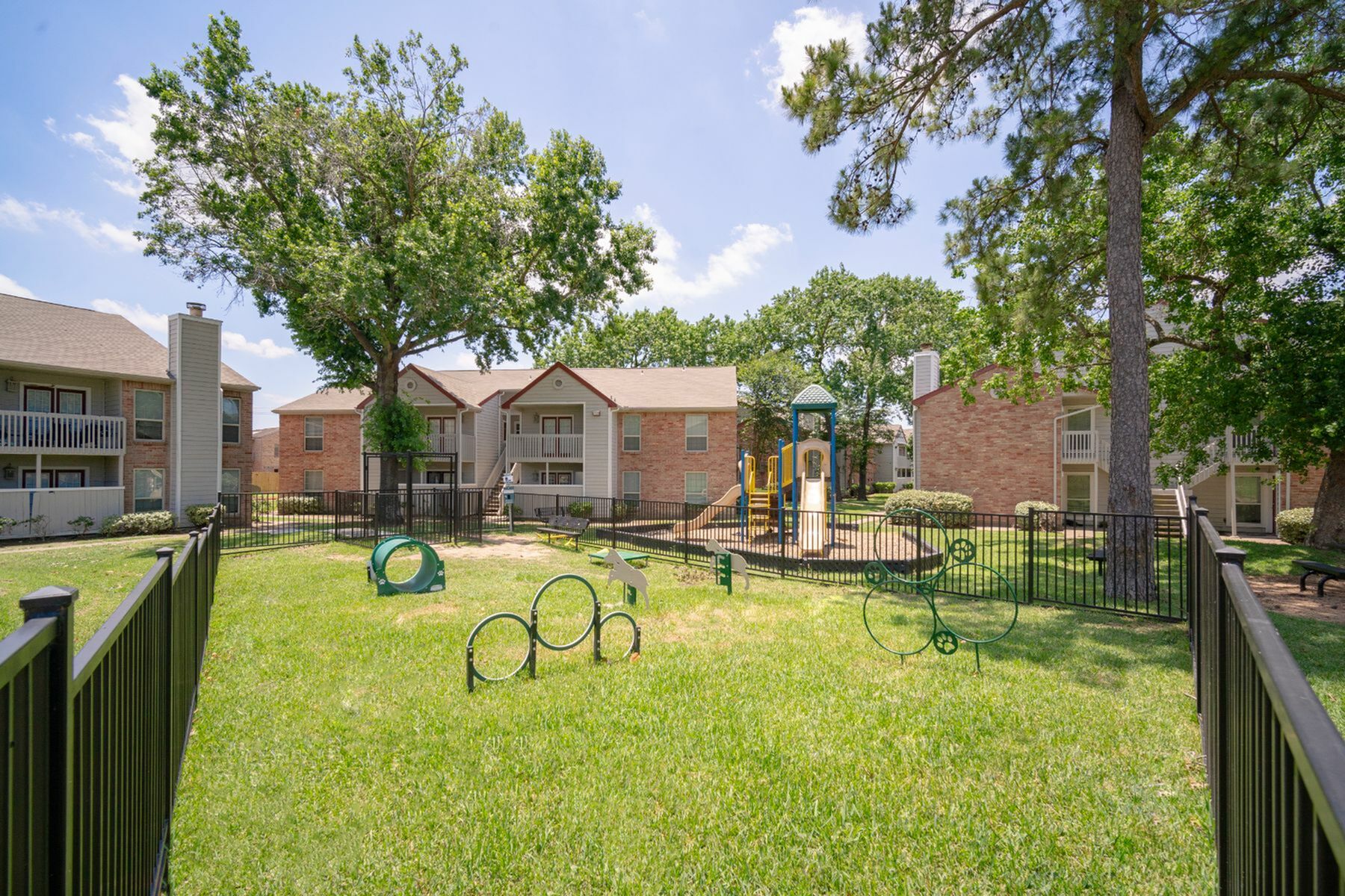 Inviting apartment complex with modern exteriors, lush green lawn, and a vibrant children\'s playground surrounded by trees.