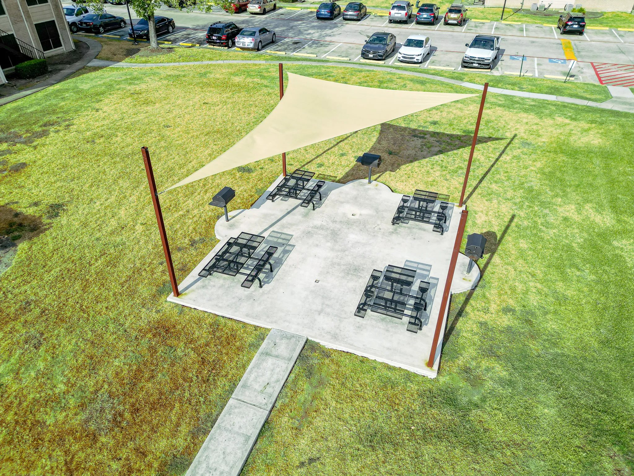 Inviting outdoor picnic area with shade sail and modern grilling stations, surrounded by lush green space.