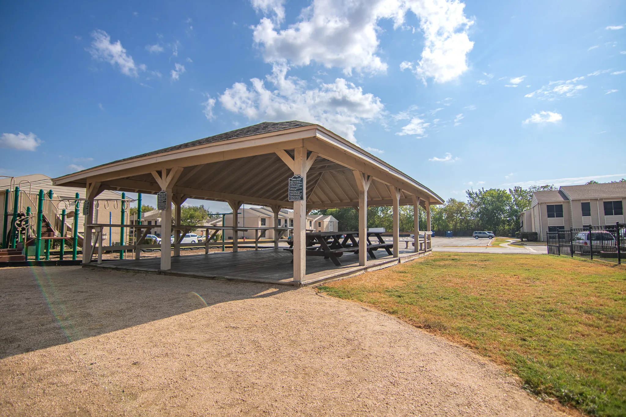 Charming outdoor gazebo with picnic tables surrounded by green spaces and a playground, perfect for gatherings and relaxation.