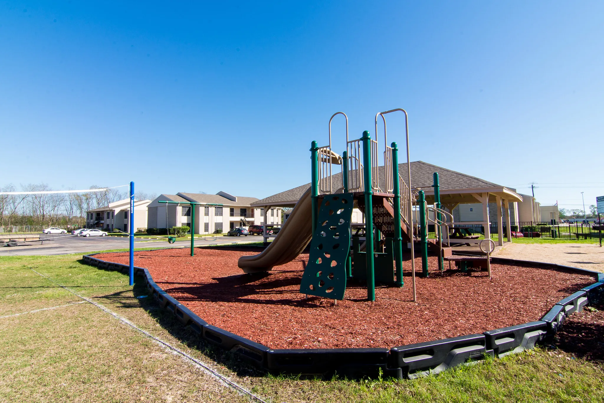 Family-friendly apartment complex showcasing a vibrant playground with slides, climbing structures, and ample green space under clear blue skies.