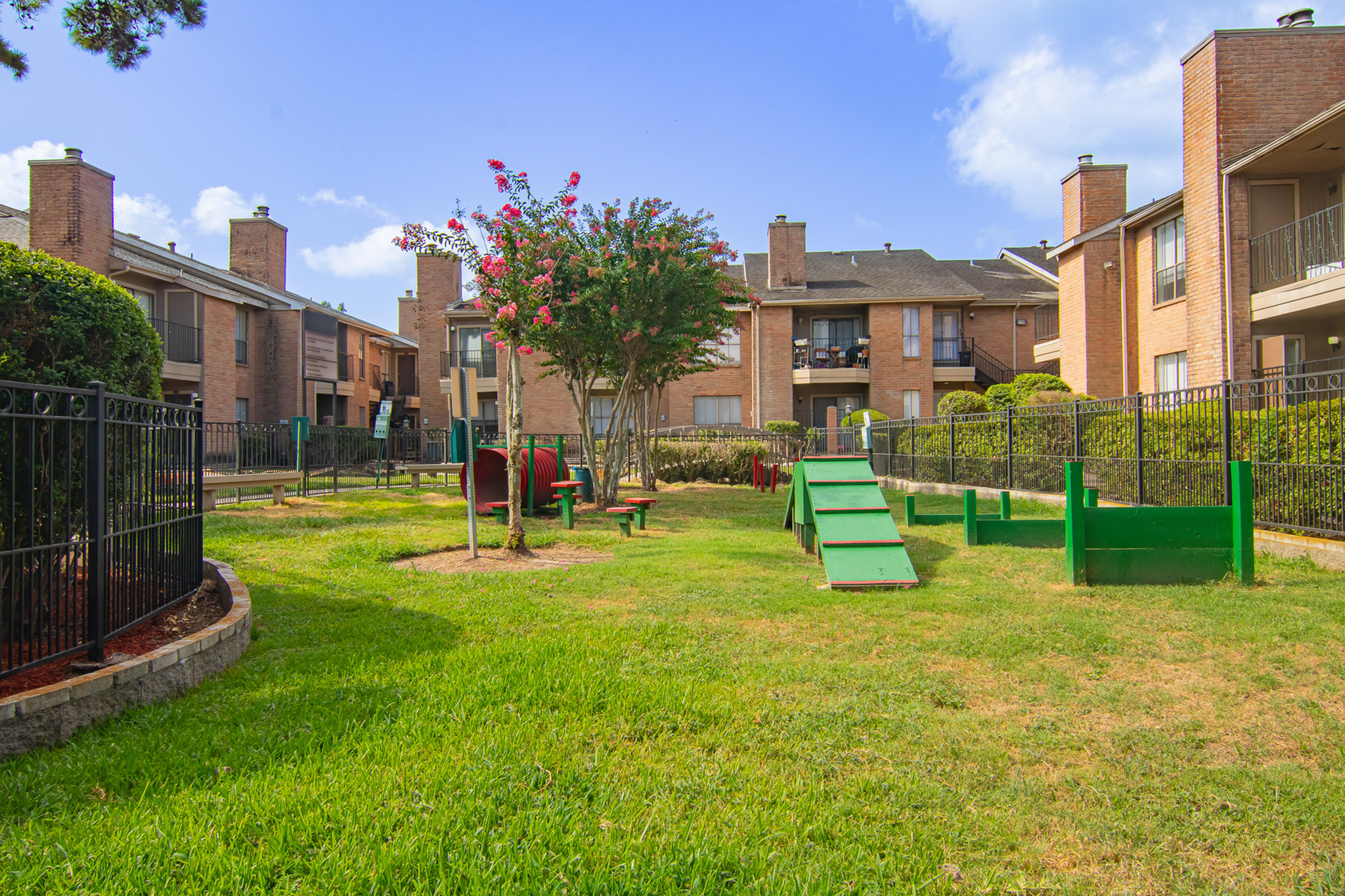 Charming apartment complex with vibrant dog park featuring agility structures and lush landscaping.
