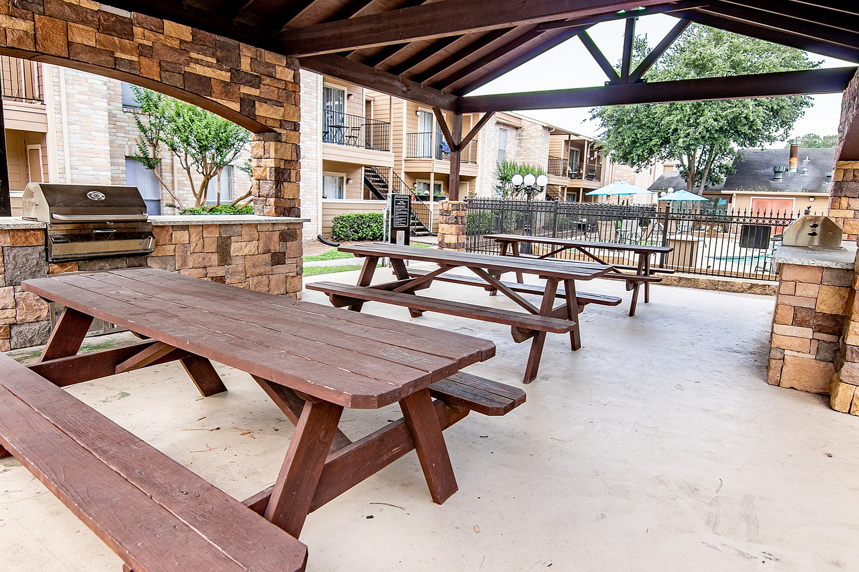 Charming outdoor pavilion with rustic wooden picnic tables and a stone barbecue area, perfect for gatherings.