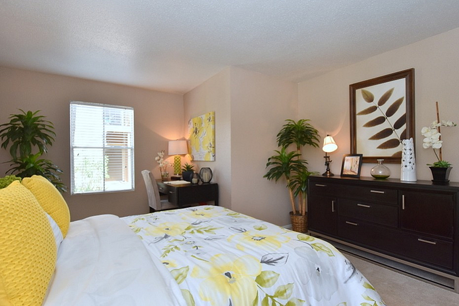 Charming bedroom with elegant decor, featuring a cozy bed with vibrant yellow accents and a stylish workspace by the window.