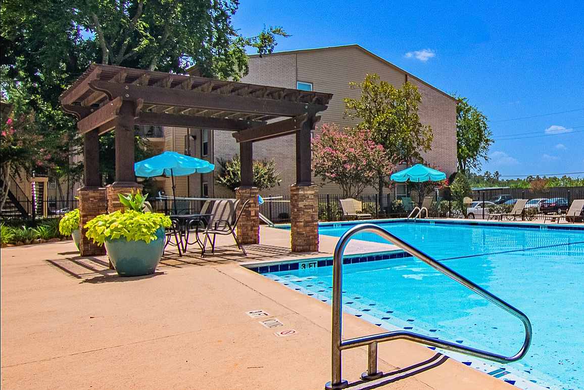 Inviting outdoor pool area with sun loungers and pergola-shaded seating, surrounded by lush trees and vibrant landscaping.