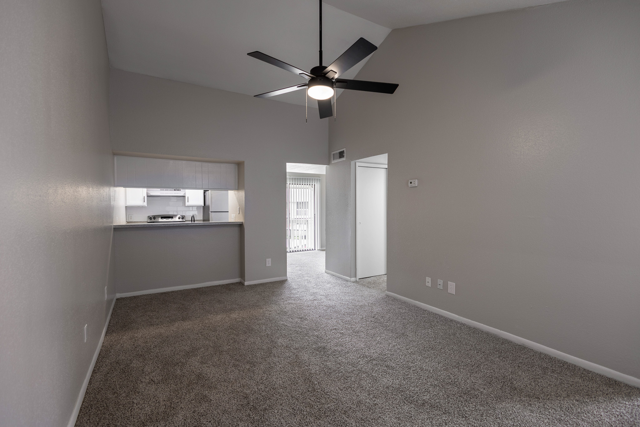 Bright living area with vaulted ceiling and modern fan, adjoining kitchen pass-through with sleek appliances.