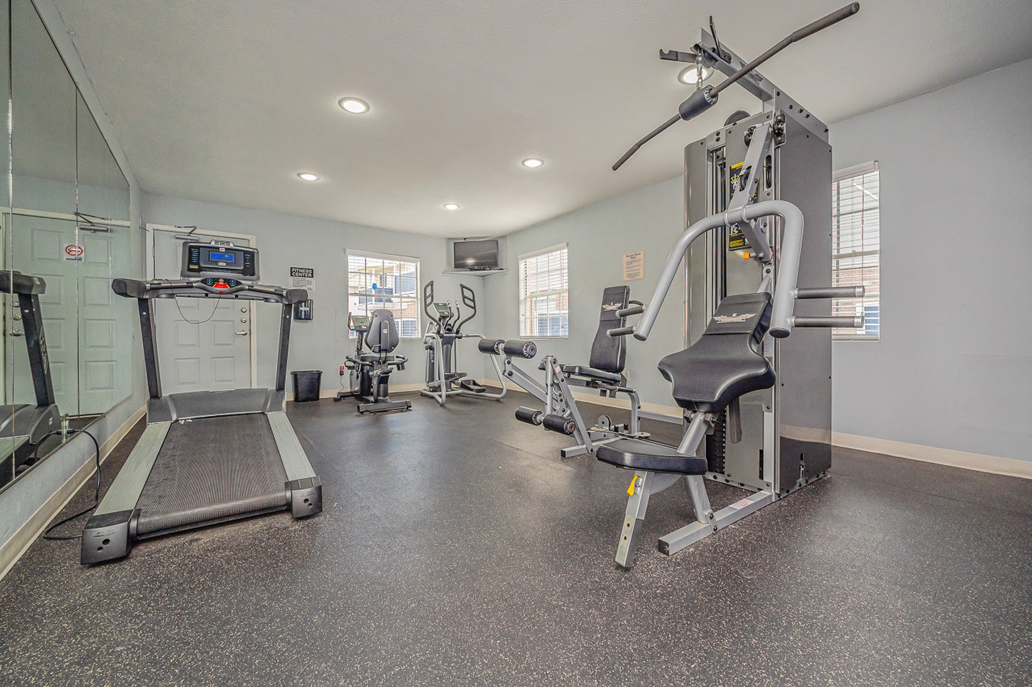 Contemporary apartment gym equipped with treadmill, exercise bike, and multi-functional weight machine, offering a bright and motivating workout space.