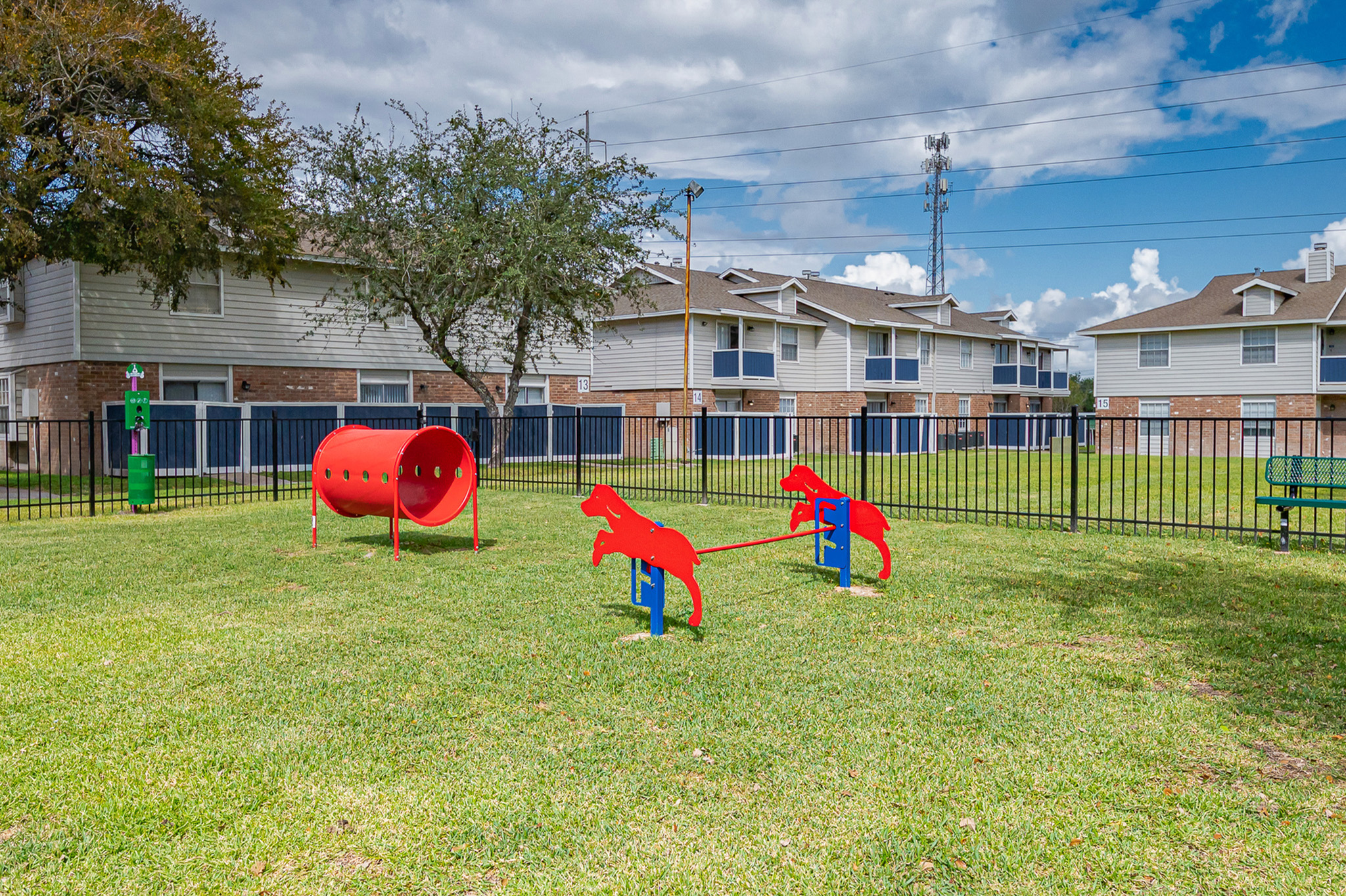 Inviting apartment community featuring a fenced-in dog park with vibrant red agility equipment and spacious grassy areas, perfect for pet enthusiasts.