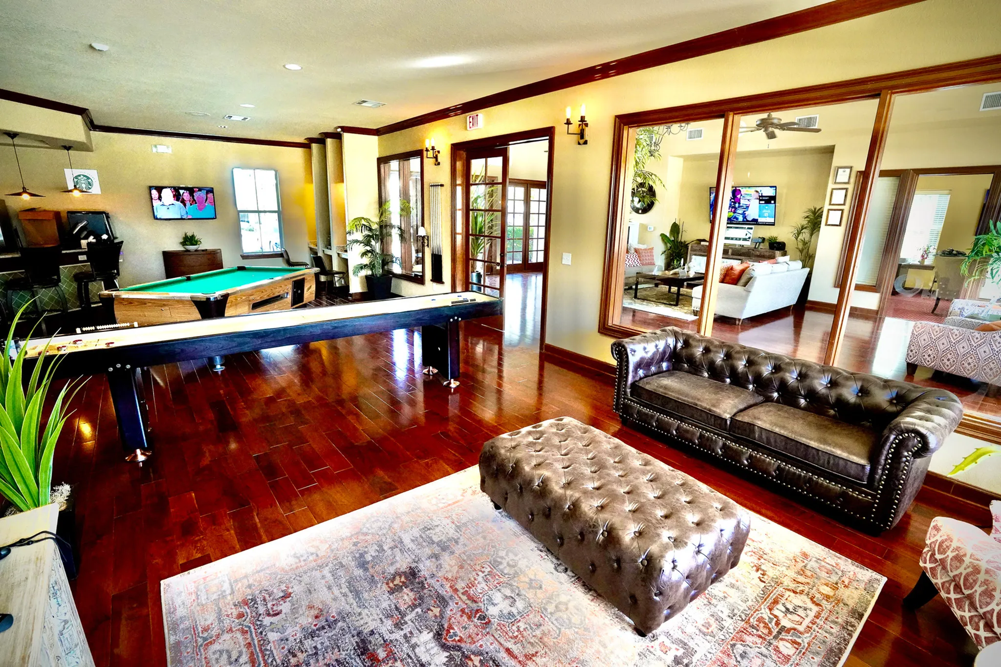 Luxurious apartment interior featuring a chic game room with a pool table and shuffleboard, alongside a sophisticated leather seating area adjacent to a cozy living space.