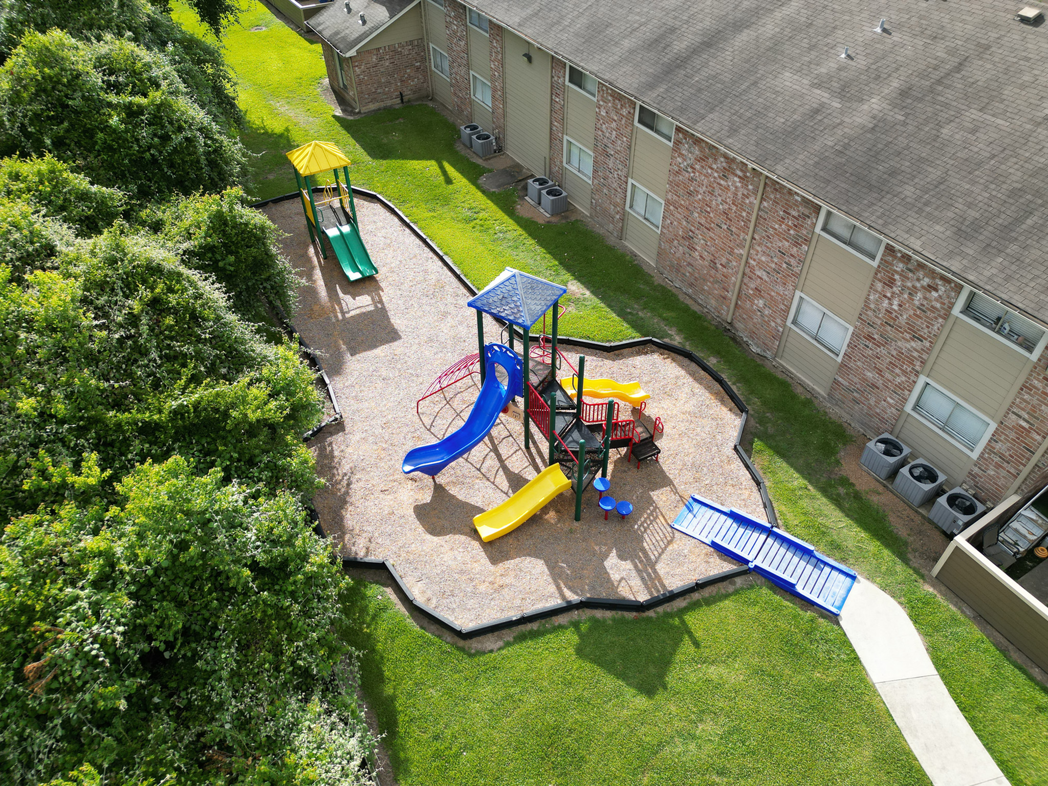 Charming apartment complex with vibrant playground, featuring colorful slides and climbing structure, surrounded by lush greenery.
