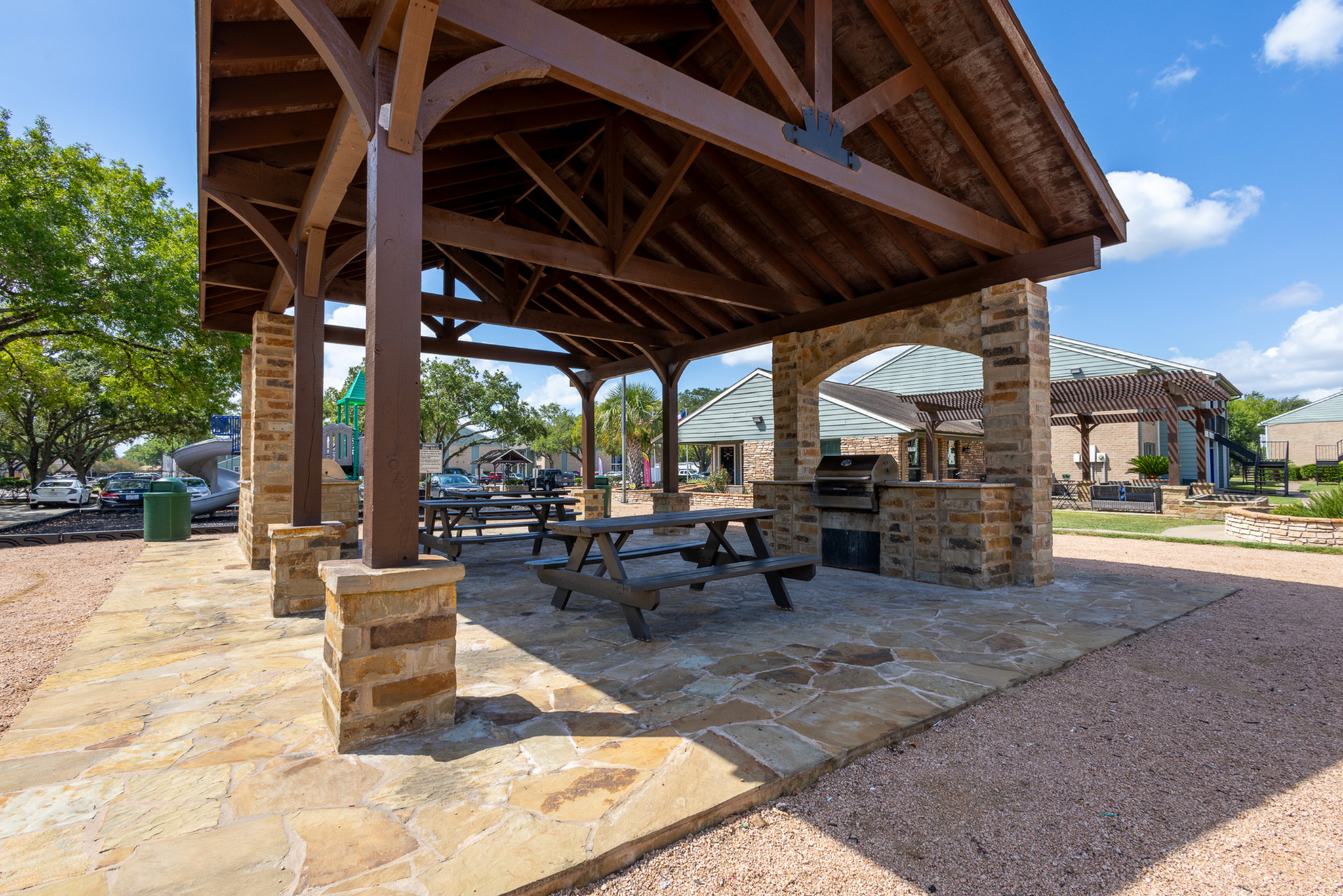 Charming outdoor pavilion area with stone flooring, sturdy wooden beams, and picnic tables, ideal for gatherings and enjoying the serene surrounding greenery.