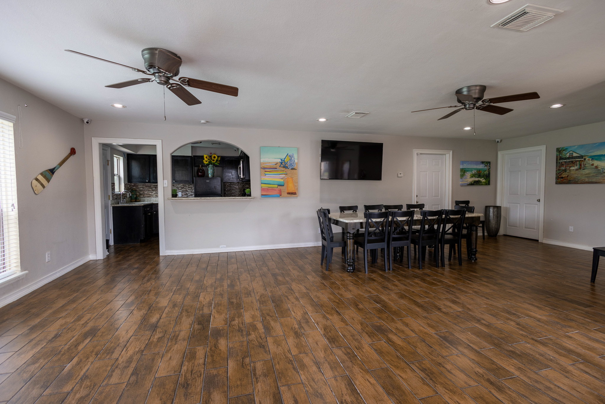Inviting open-concept living room with wooden flooring, modern ceiling fans, and elegant dining area connected to a stylish kitchen.