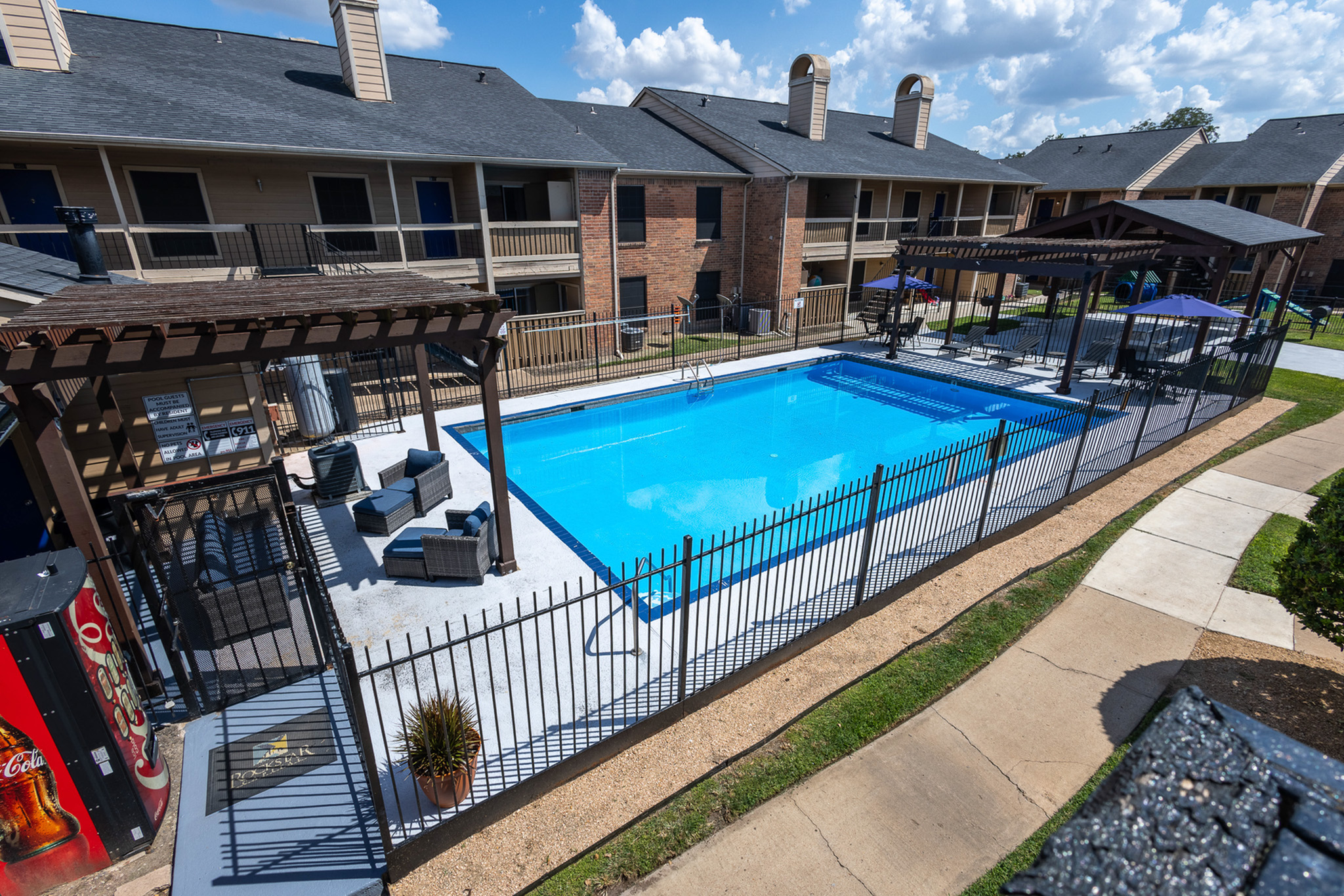 Charming apartment complex boasting a pristine outdoor pool with stylish lounging areas and vibrant communal spaces, perfect for relaxation under sunny skies.