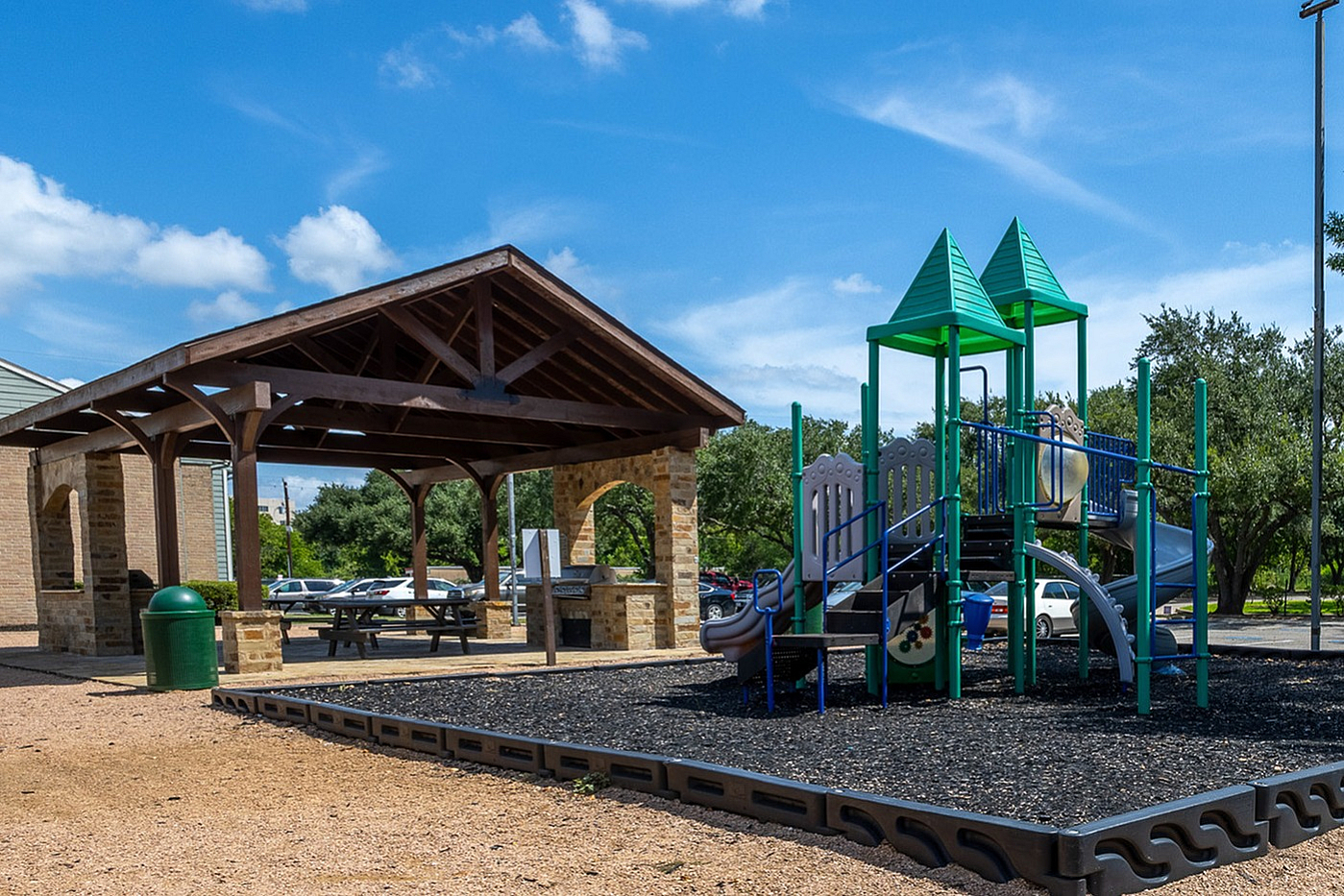 Charming outdoor playground with a slide and climbing structure, set beside a cozy picnic area under a wooden pavilion, perfect for family gatherings on a sunny day.
