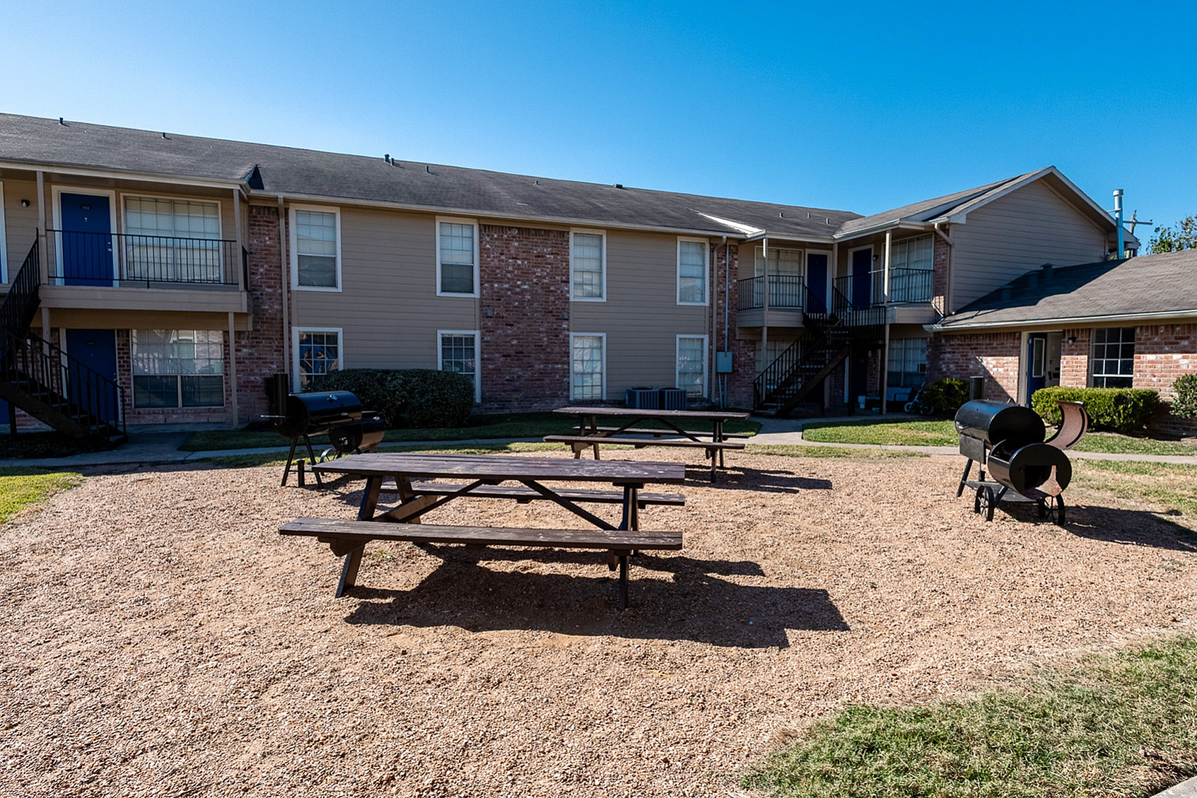Inviting apartment complex courtyard featuring picnic tables and BBQ grills, perfect for outdoor gatherings.