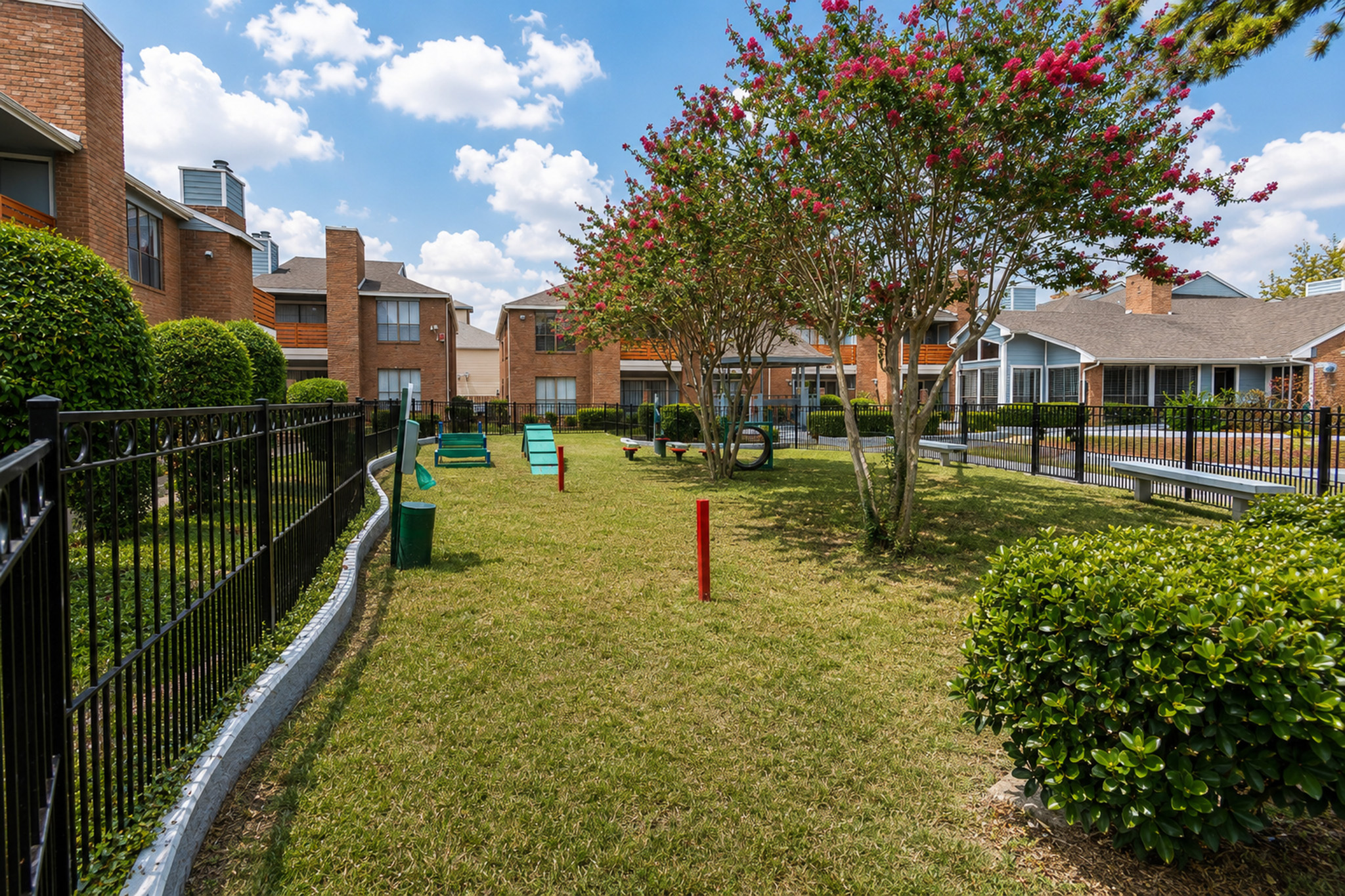 Charming landscaped courtyard with vibrant greenery and well-maintained pathways, surrounded by inviting residential buildings under a clear blue sky.