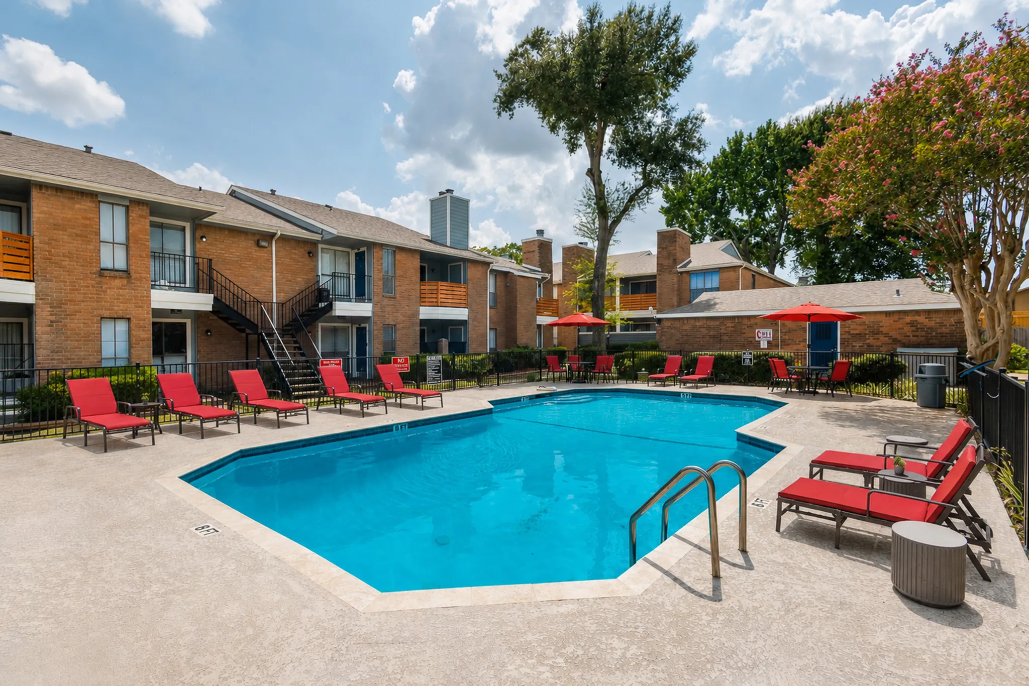Inviting apartment complex with a sparkling pool surrounded by vibrant red lounge chairs and lush greenery, perfect for relaxation.