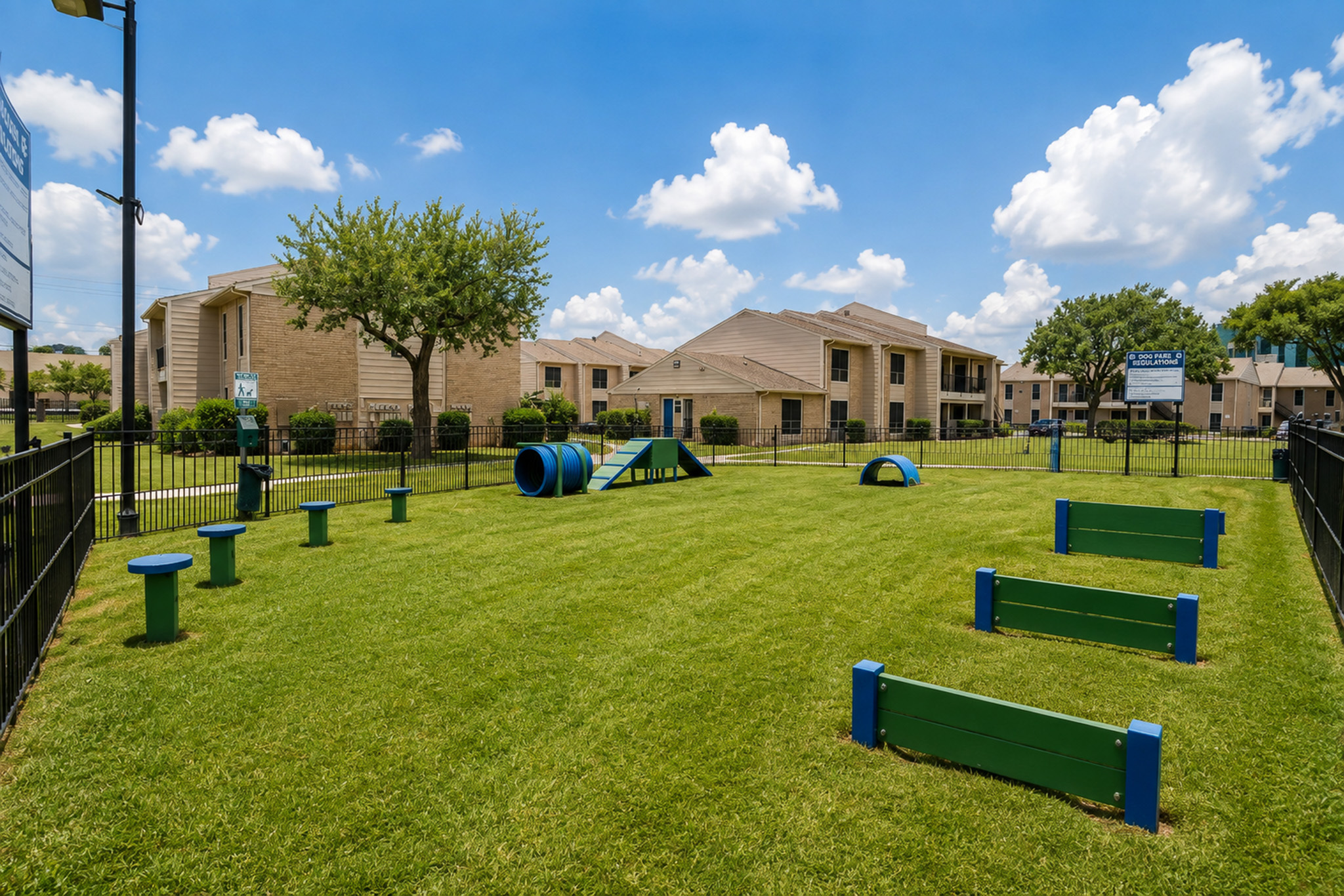 Fenced dog park with green and blue agility equipment and open lawn at The Reserve on Garth apartments in Baytown, TX.