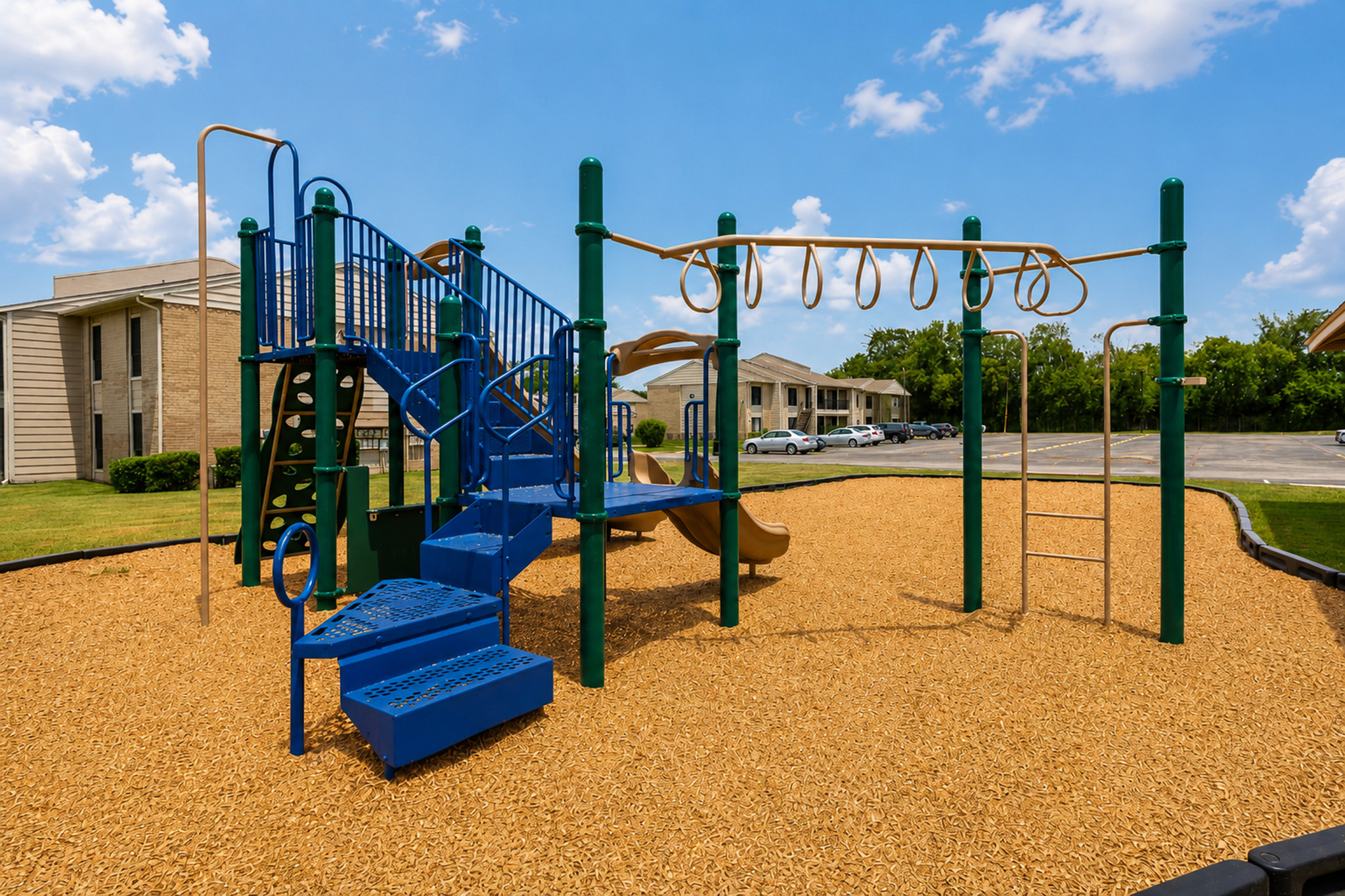 Community playground with blue, green and tan climbing equipment, slide and overhead rings at The Reserve on Garth in Baytown, TX.
