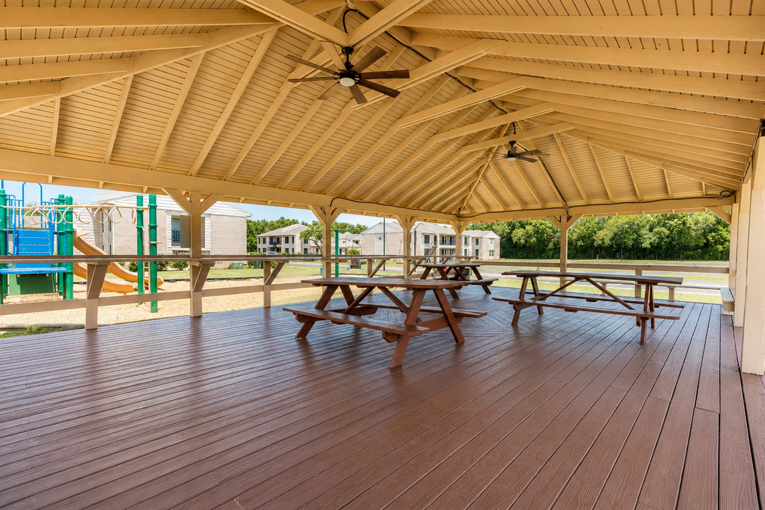 Covered community picnic pavilion with multiple picnic tables and views of the playground at The Reserve on Garth apartments in Baytown, TX.
