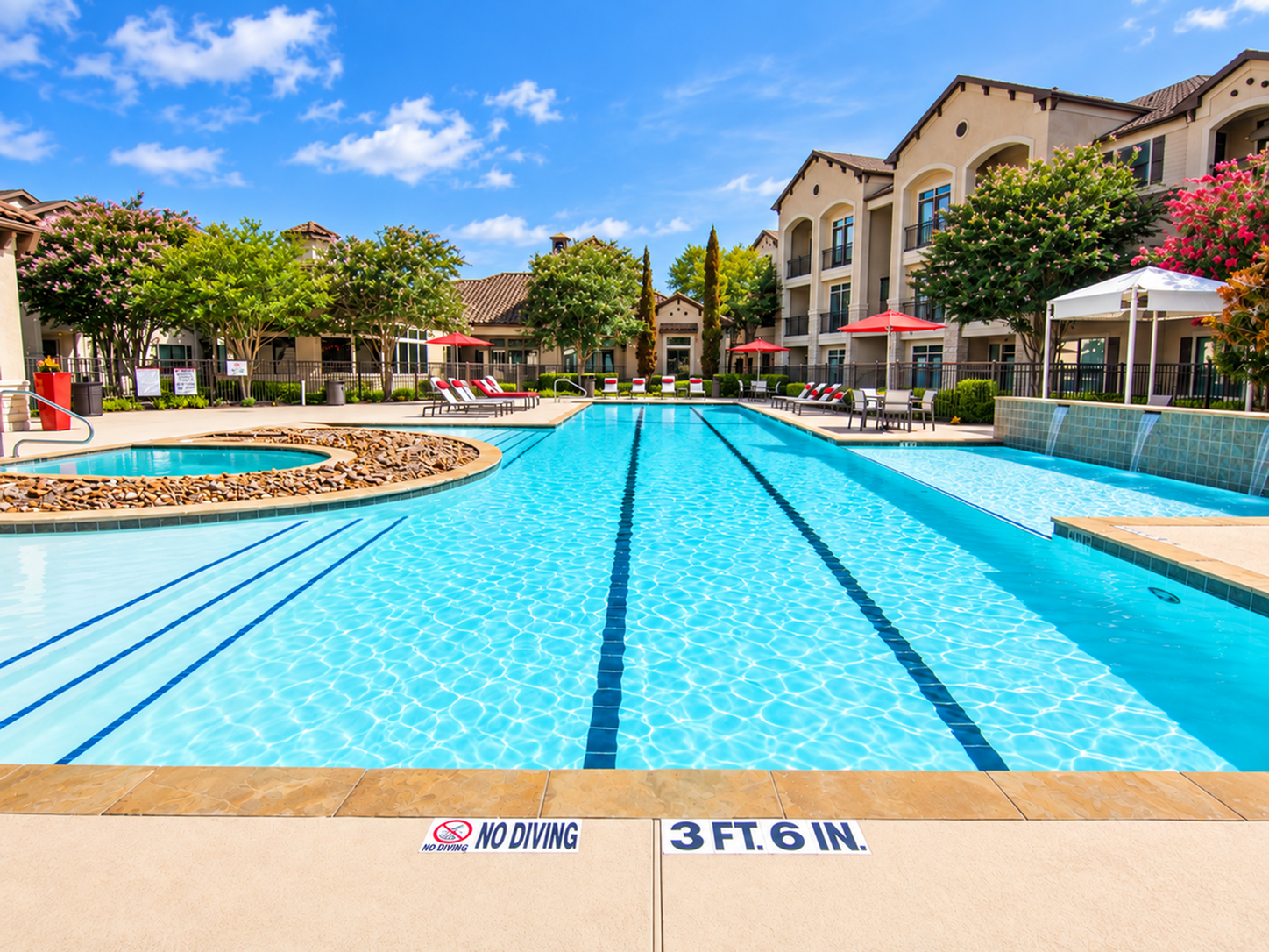 Pool and patio seating at Valencia Place apartments in Houston, TX with red umbrellas, lounge chairs and landscaped surroundings.