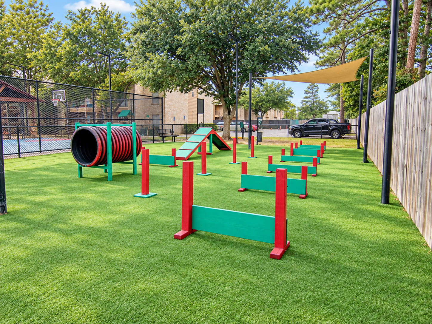 Vibrant outdoor dog park with agility equipment, lush green lawn, and shaded seating area.