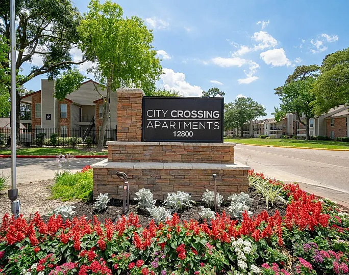 Charming entrance of City Crossing Apartments with blooming flower beds and modern architecture, offering a welcoming community vibe.