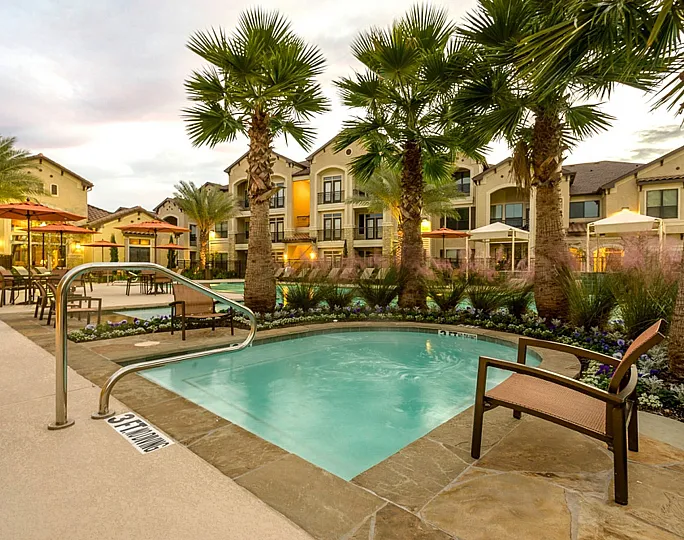 Luxurious apartment complex with inviting swimming pool, surrounded by palm trees and vibrant landscaping, perfect for relaxation.