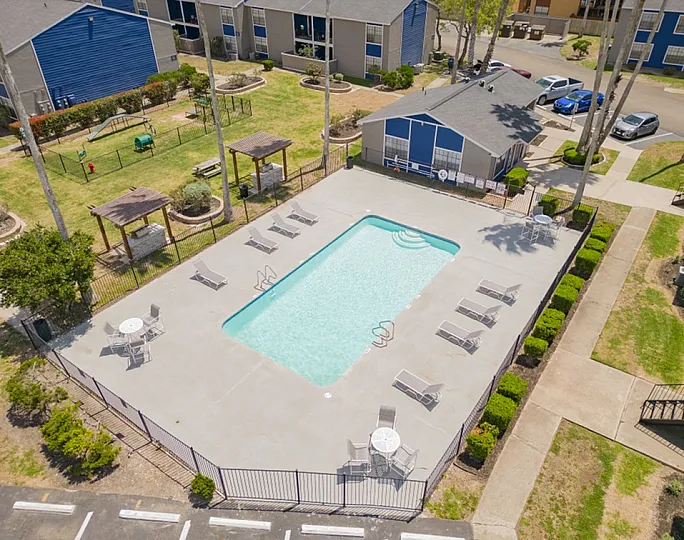 Inviting aerial view of a modern apartment complex featuring a sparkling swimming pool, surrounded by relaxing lounge chairs and lush greenery, perfect for outdoor leisure and enjoyment.