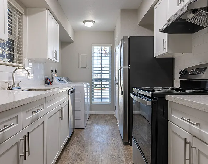 Bright and modern kitchen with sleek white cabinetry, stainless steel appliances, and in-unit laundry facilities.