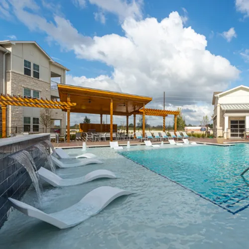 Luxurious apartment complex with a sparkling pool, elegant water features, and modern poolside loungers under a pristine sky.