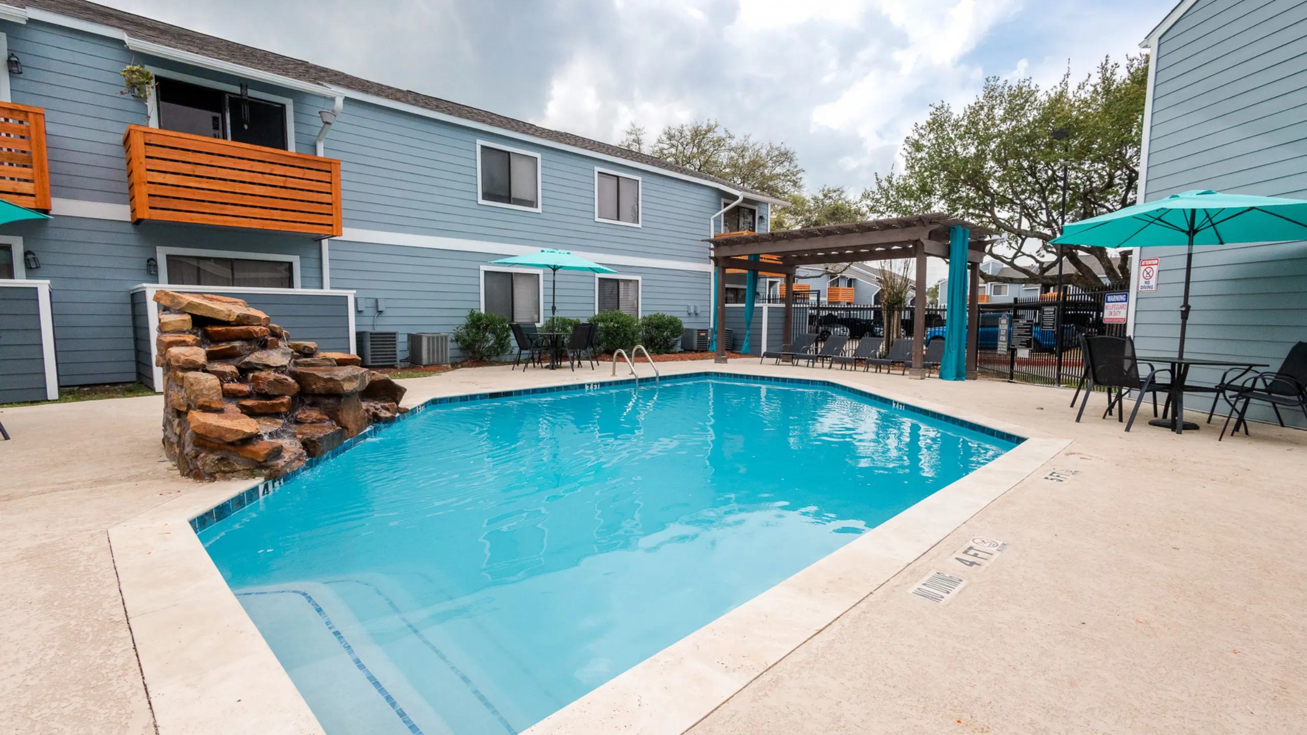 Charming apartment complex featuring a refreshing outdoor pool with relaxing lounge chairs and shaded seating areas.