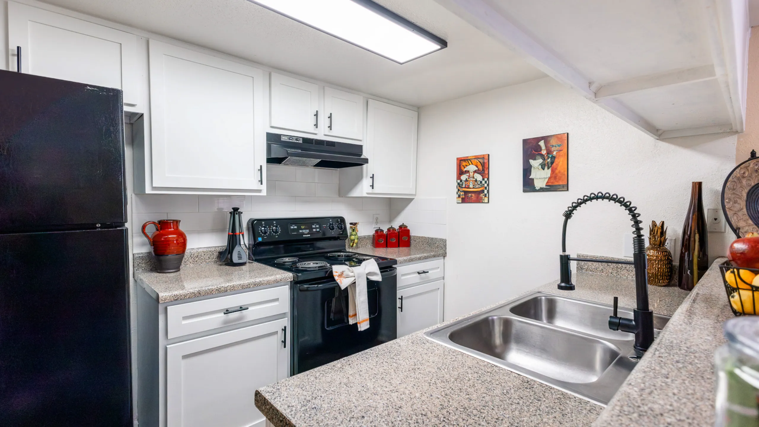 Modern kitchen with sleek black appliances, granite countertops, and stylish white cabinets, accented by vibrant decor pieces.