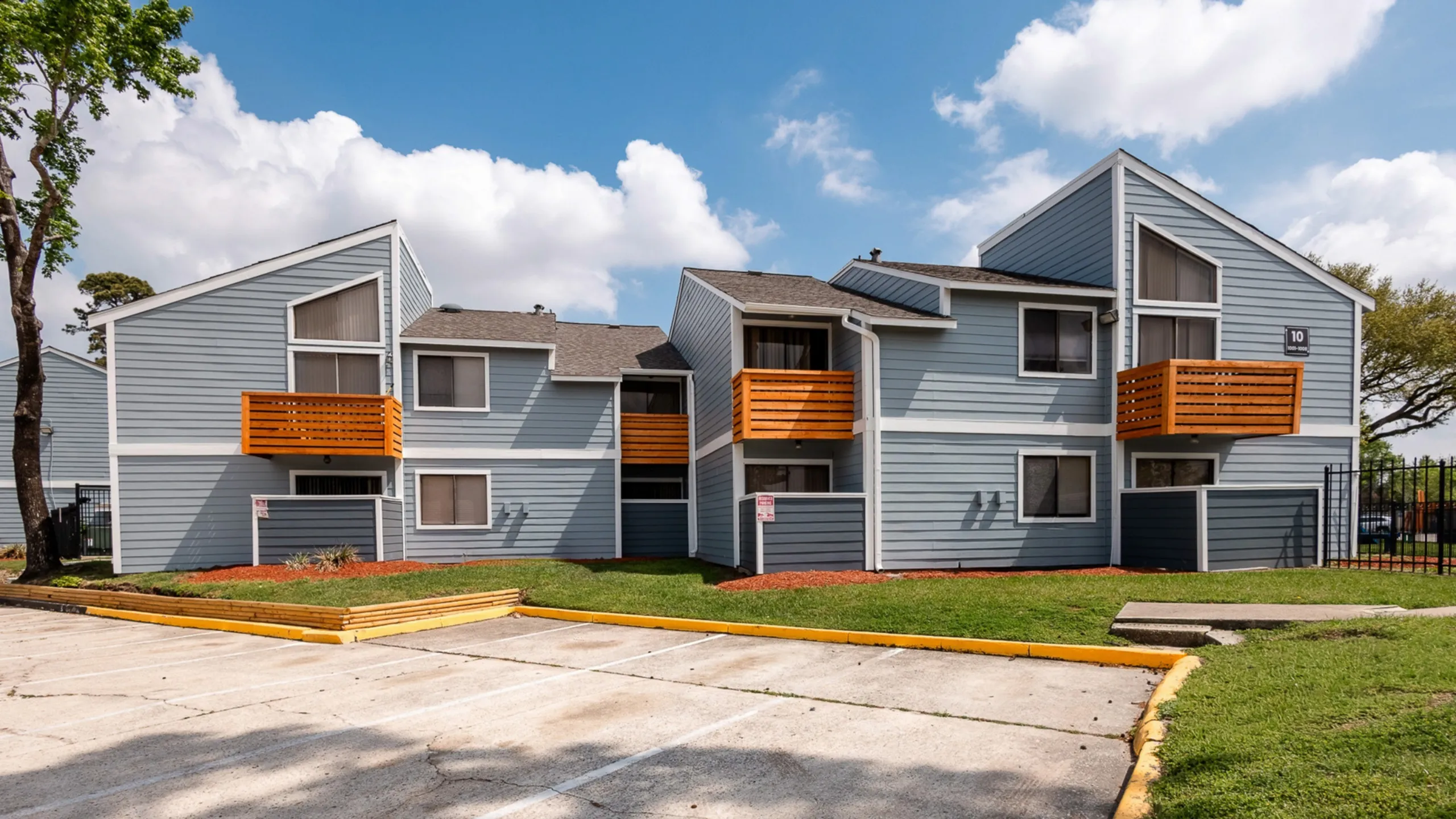 Charming multi-level apartment building with modern blue siding and vibrant orange balconies, set against a clear blue sky with lush green landscaping.