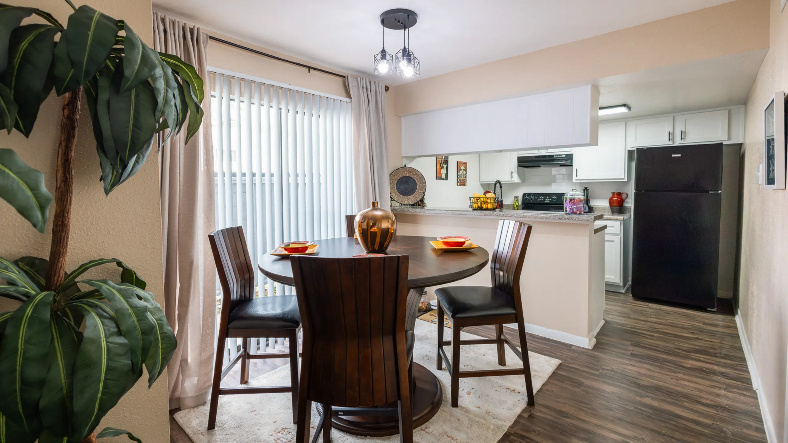 Charming dining area with elegant dark wood table set for four, open to a modern white kitchen with sleek appliances.
