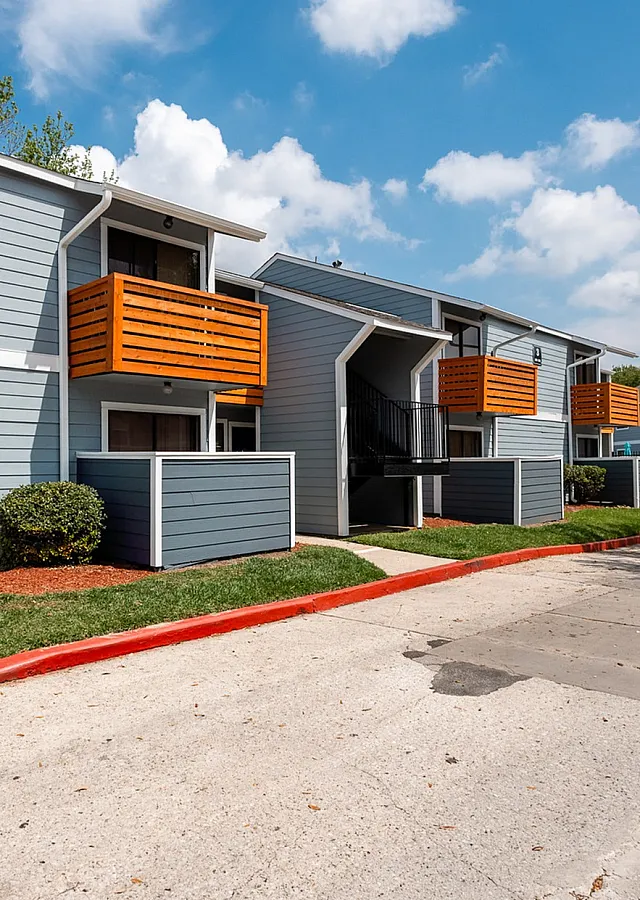 Charming apartment complex with modern gray exteriors and vibrant orange accents, surrounded by lush greenery and a clear blue sky.