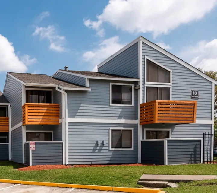 Charming two-story apartment building with modern wooden balconies and sleek blue siding on a sunny day.
