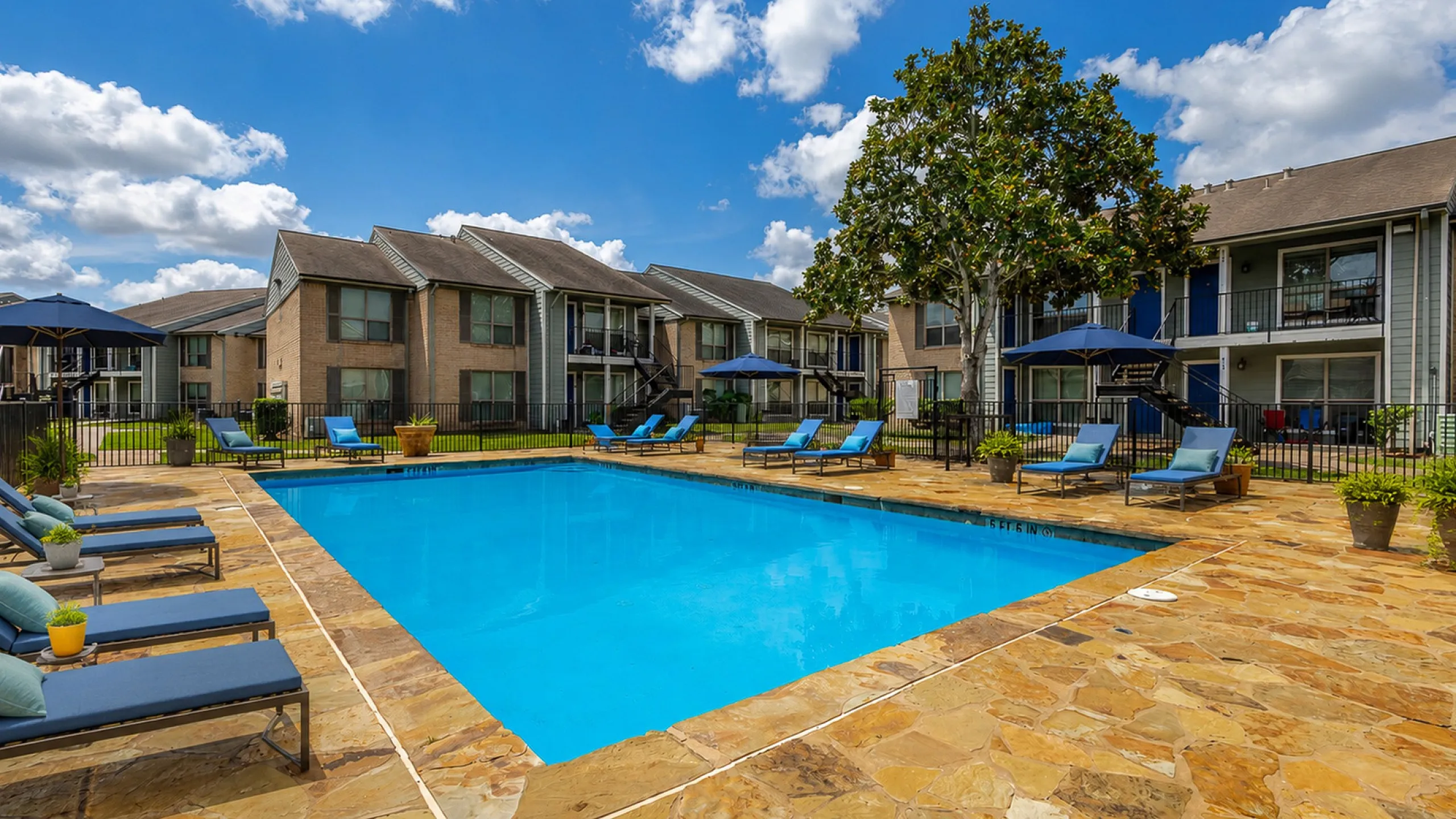 Inviting apartment complex featuring a sparkling outdoor pool, comfortable loungers, and lush greenery, perfect for relaxation and leisure.