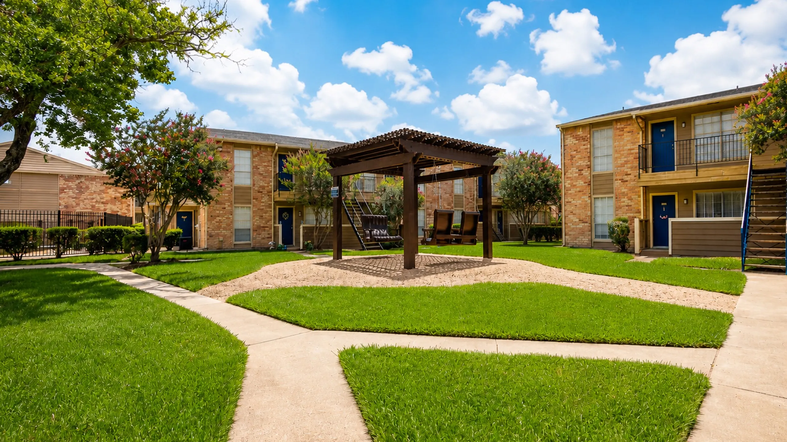 Landscaped courtyard with pergola swings and walking paths at Newport Oaks Apartments in Alvin TX