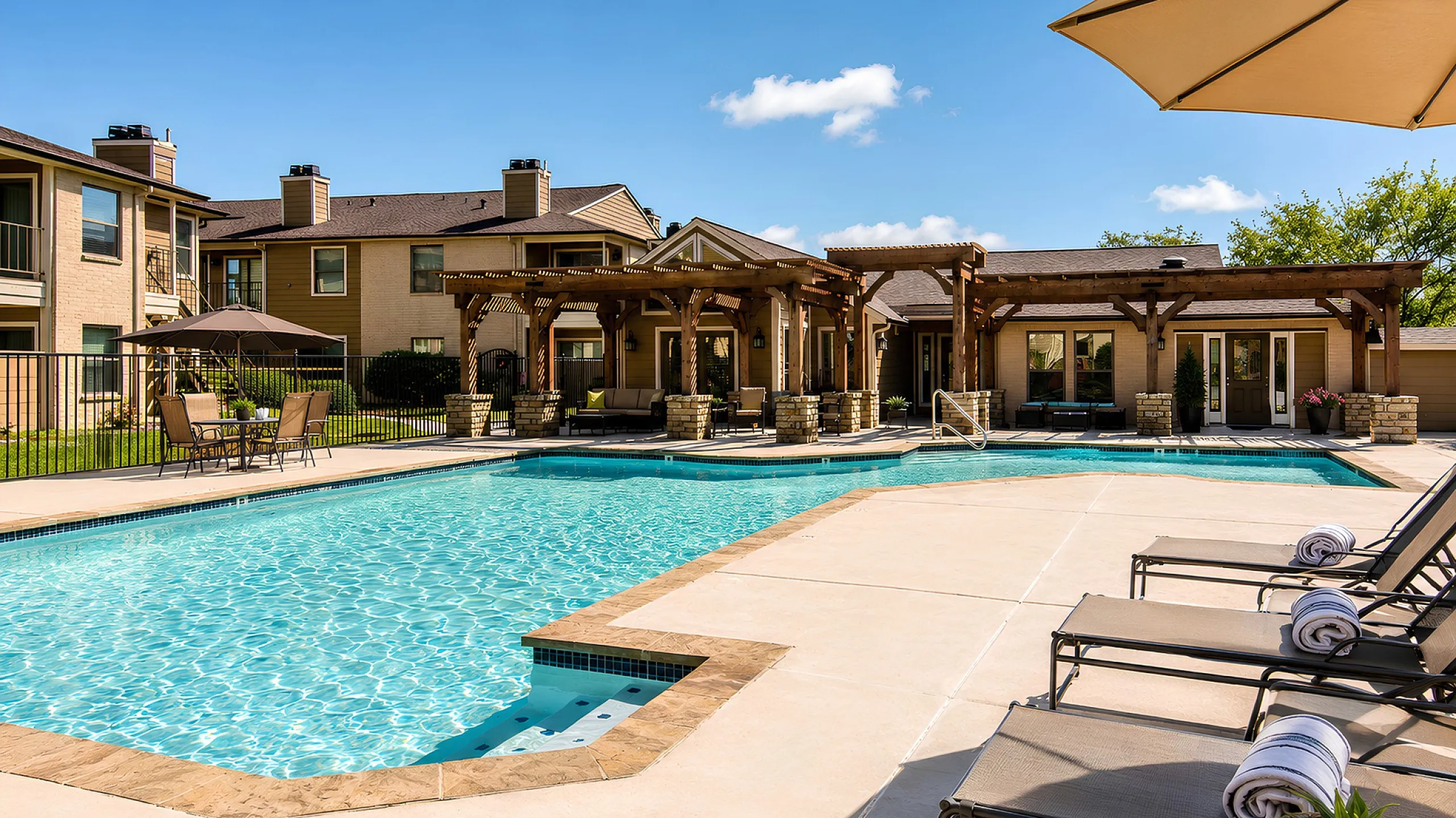 Luxurious apartment complex with a sparkling outdoor swimming pool, stylish pergola seating area, and spacious sunbathing lounge chairs.