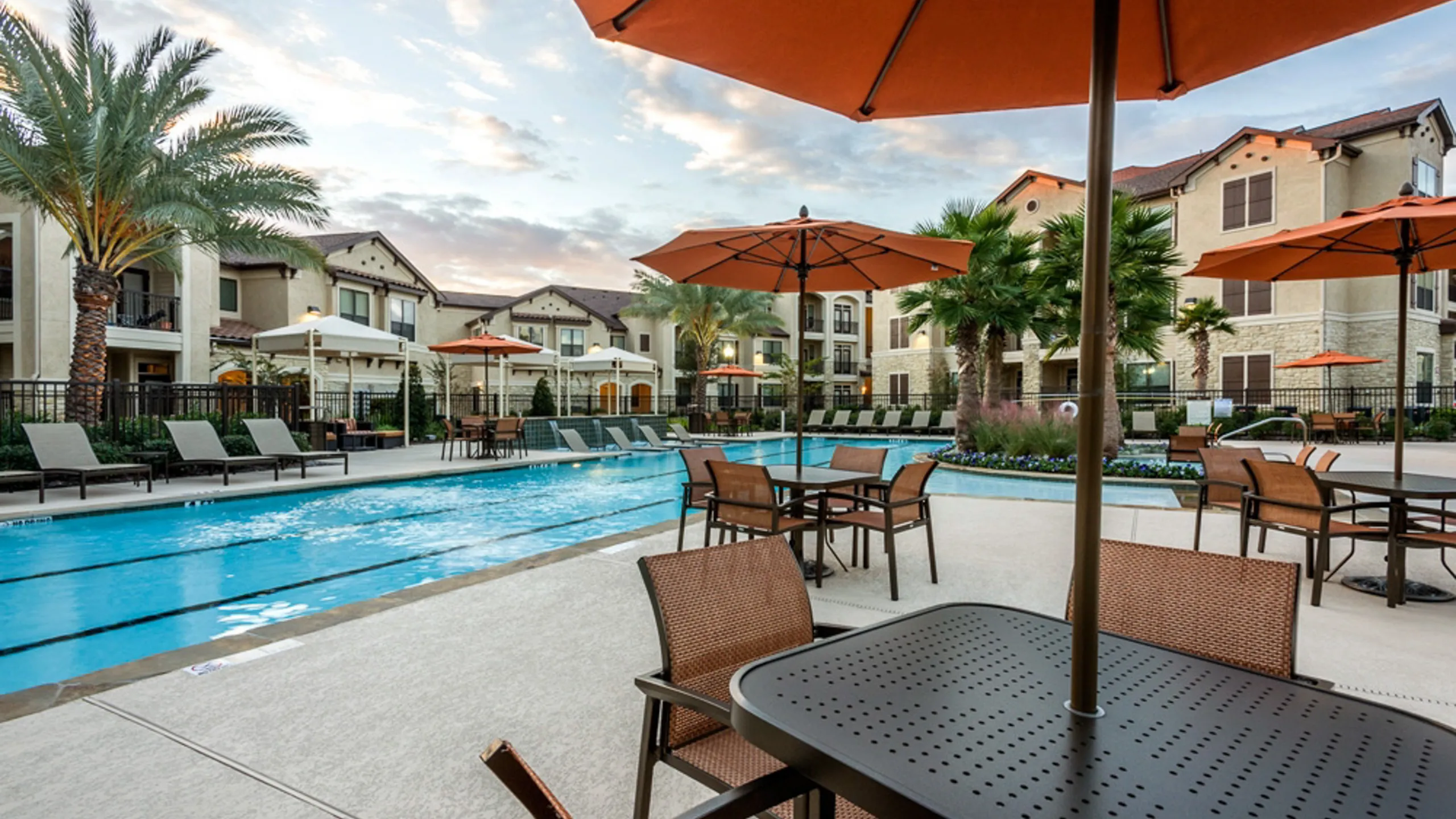 Elegant apartment complex featuring a stunning outdoor pool area with stylish umbrellas, palm trees, and comfortable seating for a luxurious lifestyle.