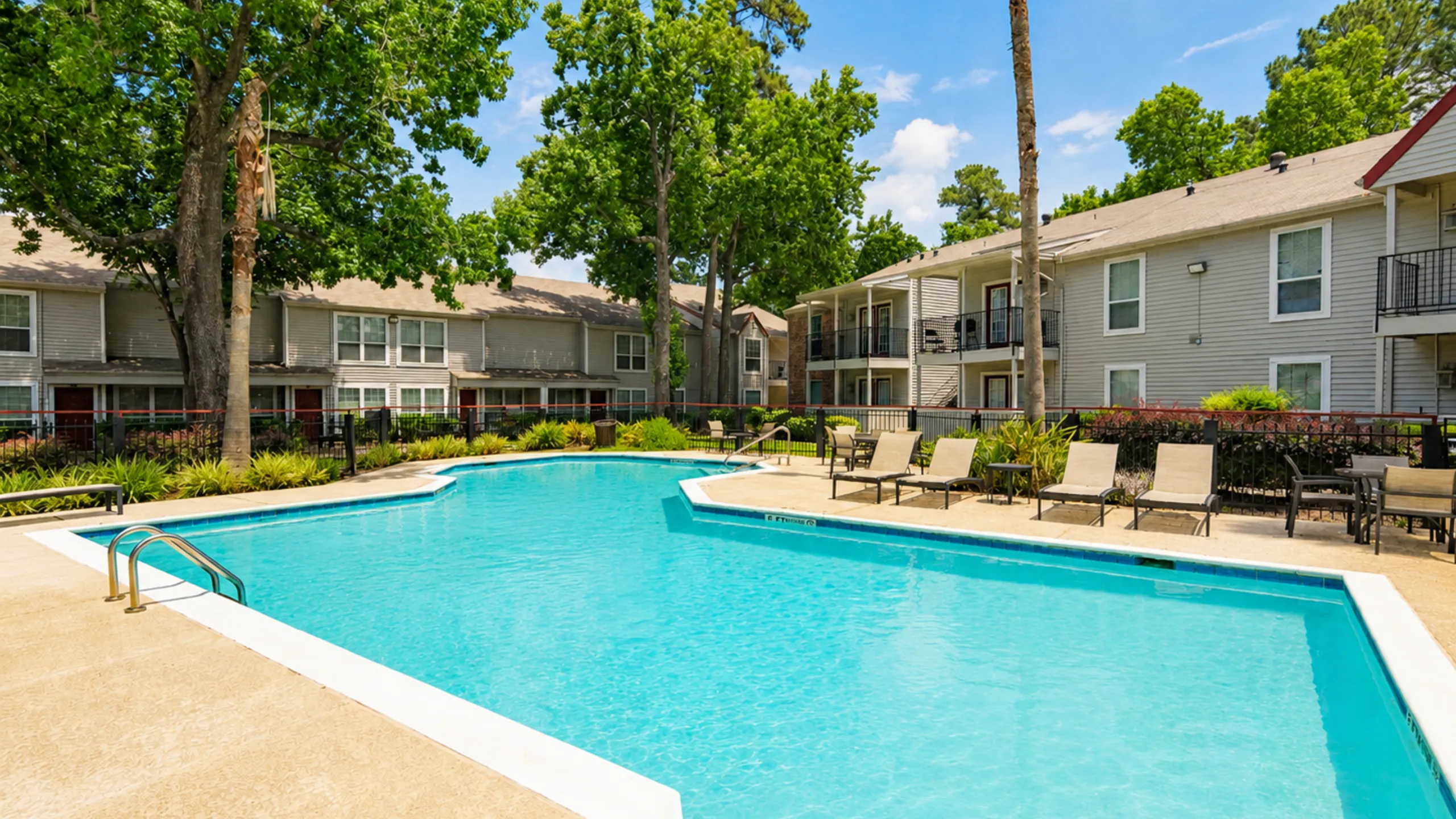 Inviting apartment complex with a sparkling pool surrounded by lush greenery and cozy lounging areas.