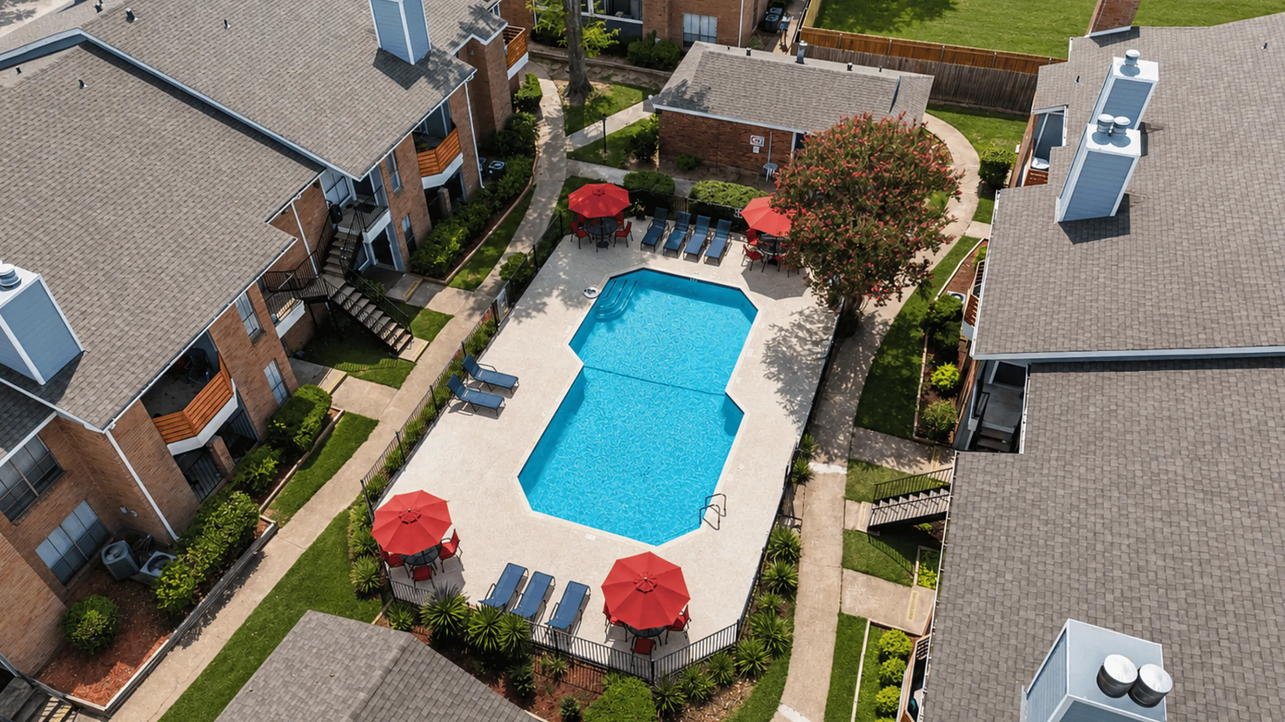 Aerial view of the Deerbrook Gardens swimming pool in Humble, TX with organized poolside seating, umbrellas and landscaped grounds.