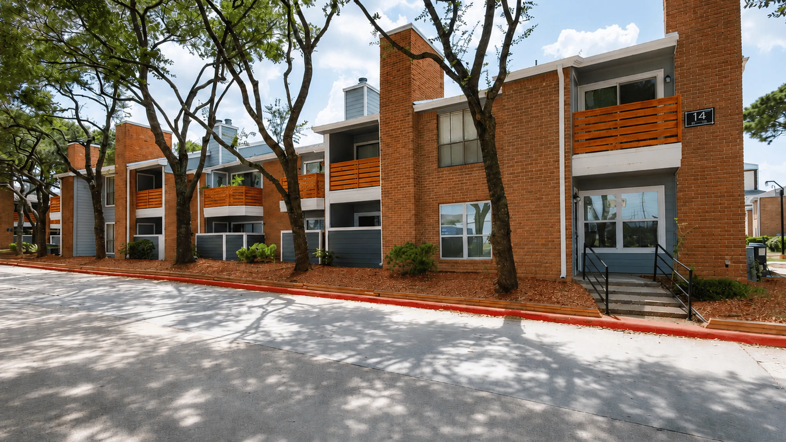 Deerbrook Gardens apartment building in Humble, TX with brick exterior, blue-gray accents, private patios and wood balconies.