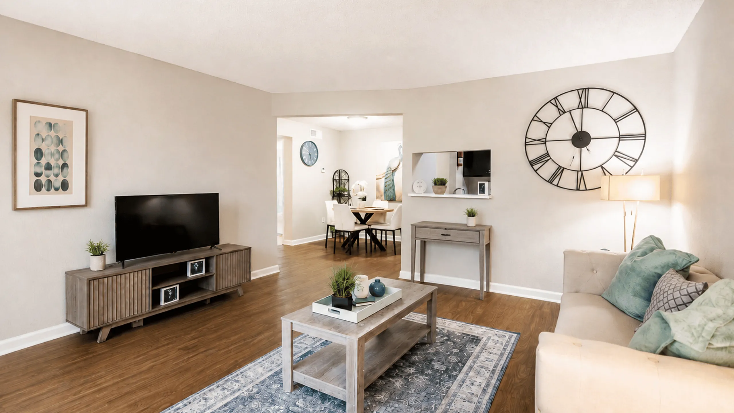 Furnished apartment living room with wood-style flooring, neutral seating, area rug and adjoining dining area at The Reserve on Garth in Baytown, TX