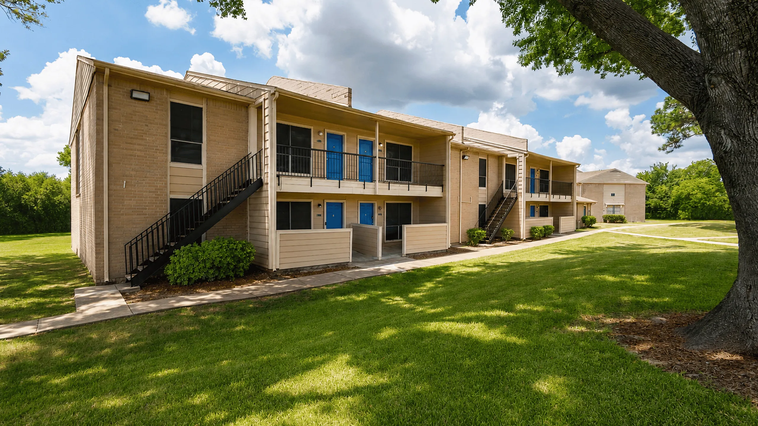 Two-story apartment building with blue entry doors, exterior staircase and landscaped grounds at The Reserve on Garth in Baytown, TX.