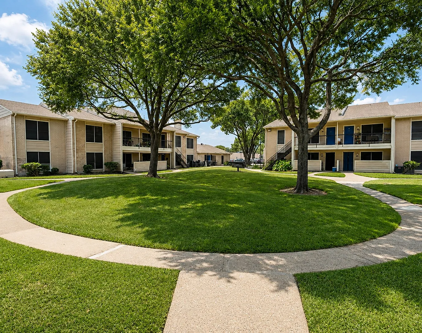 Exterior of The Reserve on Garth apartments in Baytown, TX featuring beige brick buildings, blue doors, mature trees and landscaped lawns.