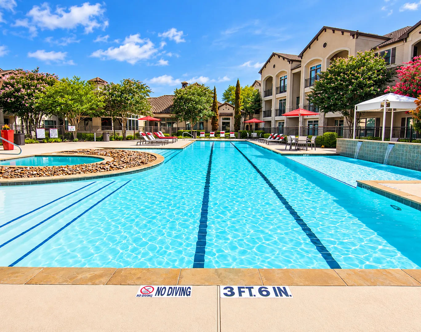 Pool and patio seating at Valencia Place apartments in Houston, TX with red umbrellas, lounge chairs and landscaped surroundings.